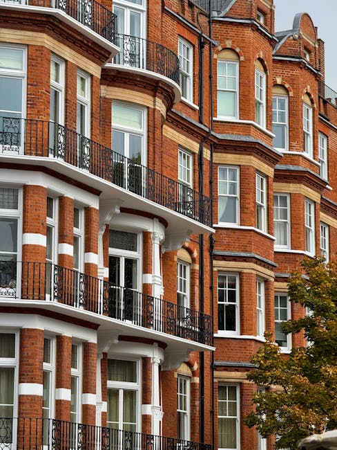 A large, historic brick building with multiple stories and a symmetrical facade, featuring white window frames and decorative architectural elements. The building is set against a clear blue sky, with